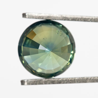 Direct pavilion-side view of the round green sapphire in tweezers, with lower facets converging to the center.