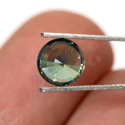 Pavilion-side view of the round green sapphire in tweezers against a fingertip for scale.