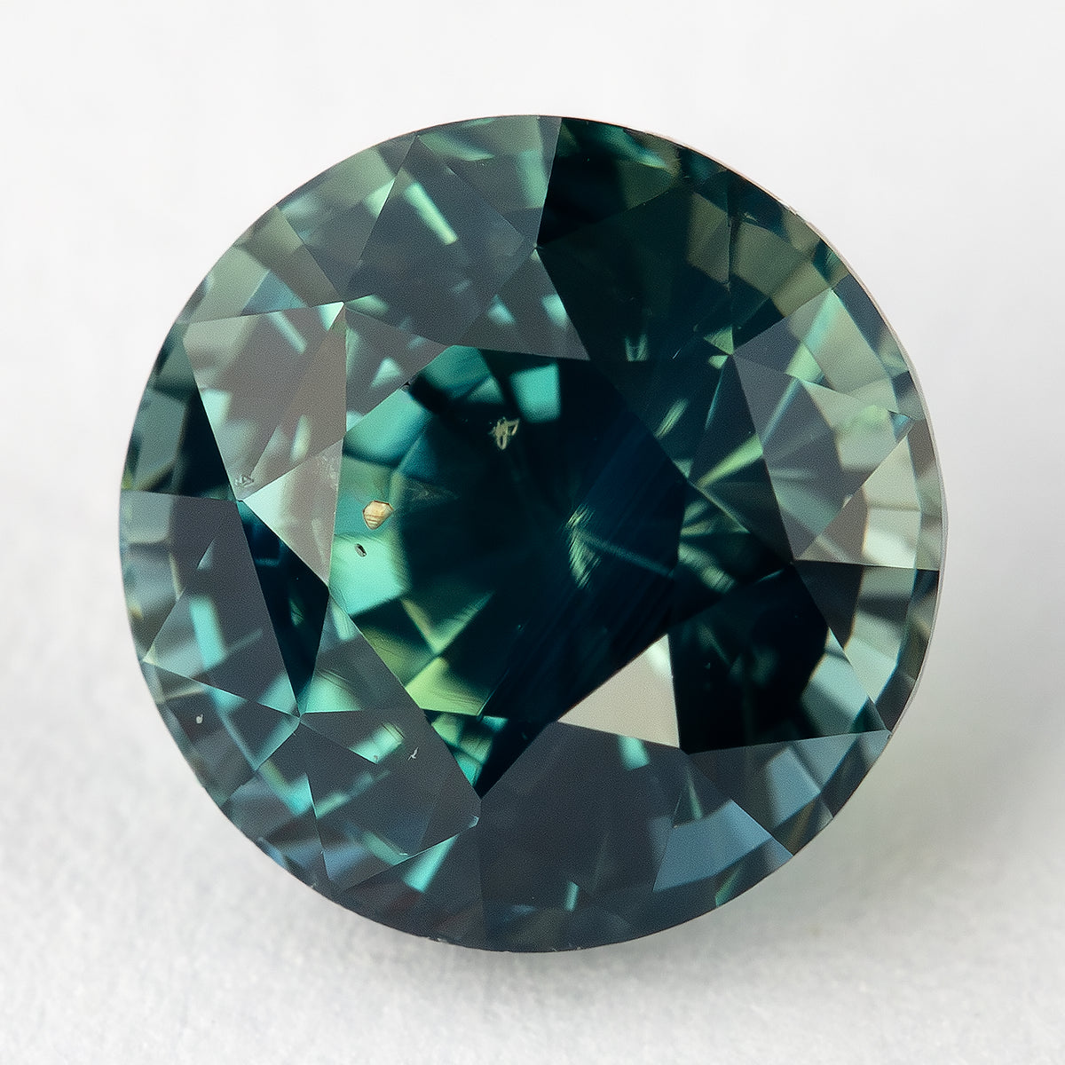 Loose round sapphire featuring deep teal and green hues.