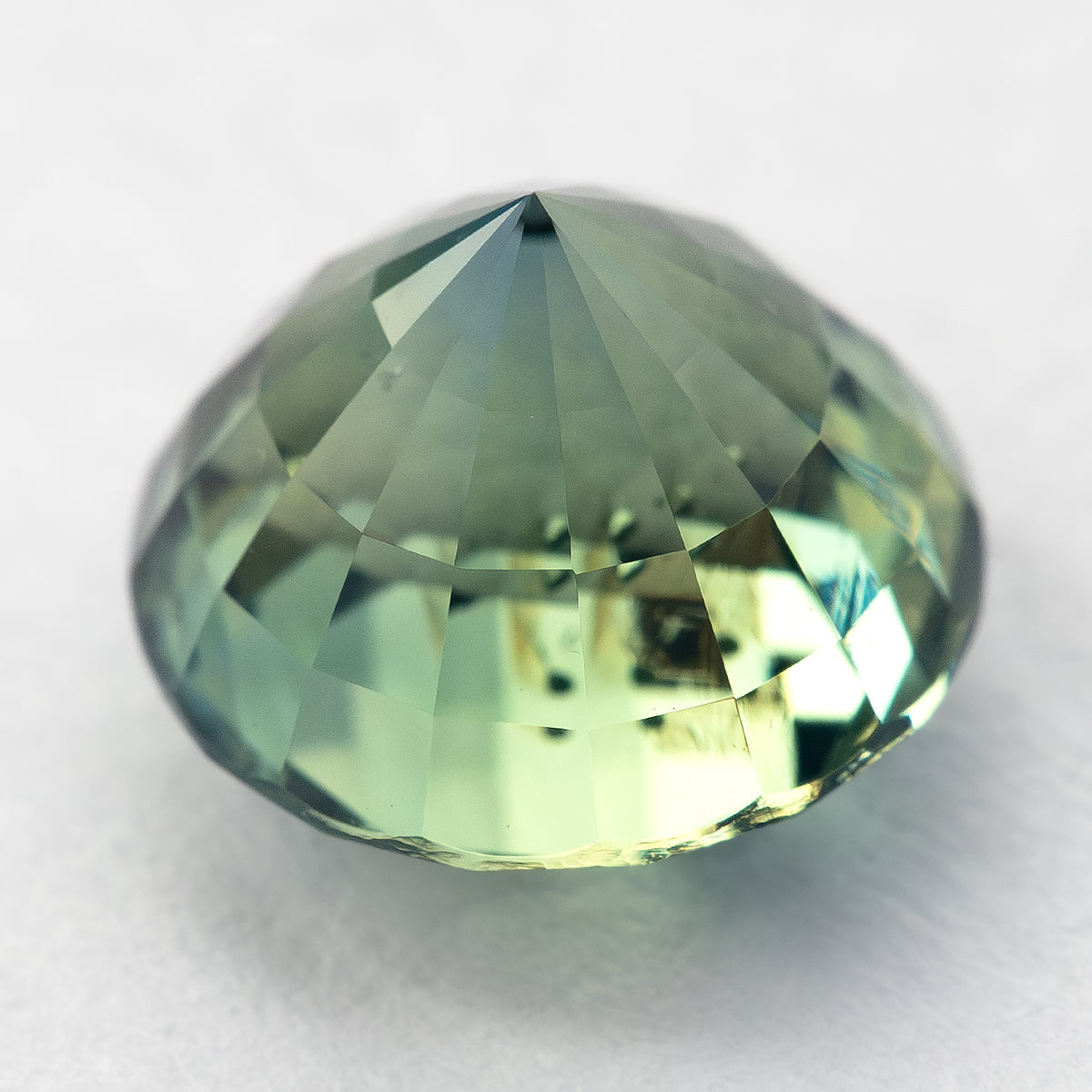 Oblique pavilion-side view of the round green sapphire resting on a light surface, showing its lower facets.