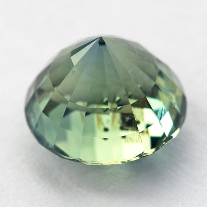 Oblique pavilion-side view of the round green sapphire resting on a light surface, showing its lower facets.