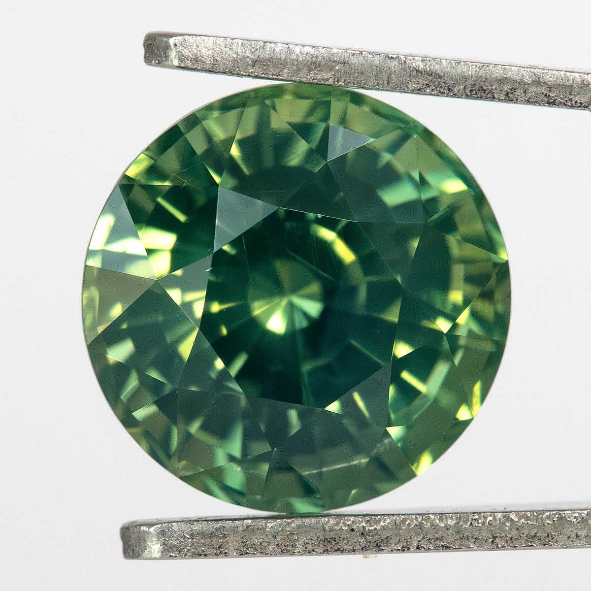 Round olive teal green sapphire held in tweezers against a white background, second perspective.