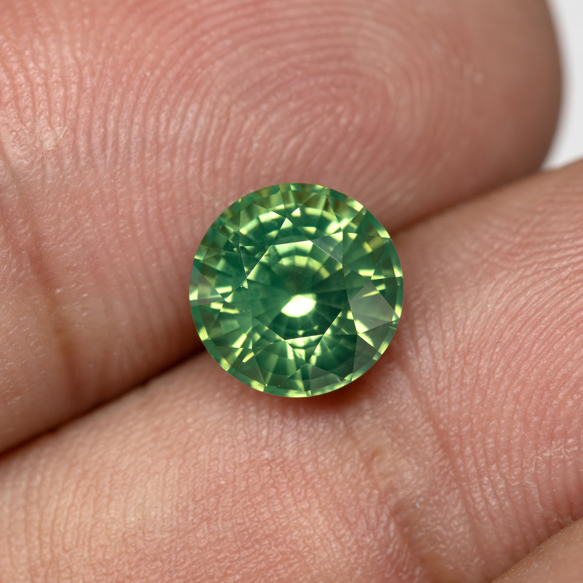Close-up scale view of a round olive teal green sapphire held between fingers.