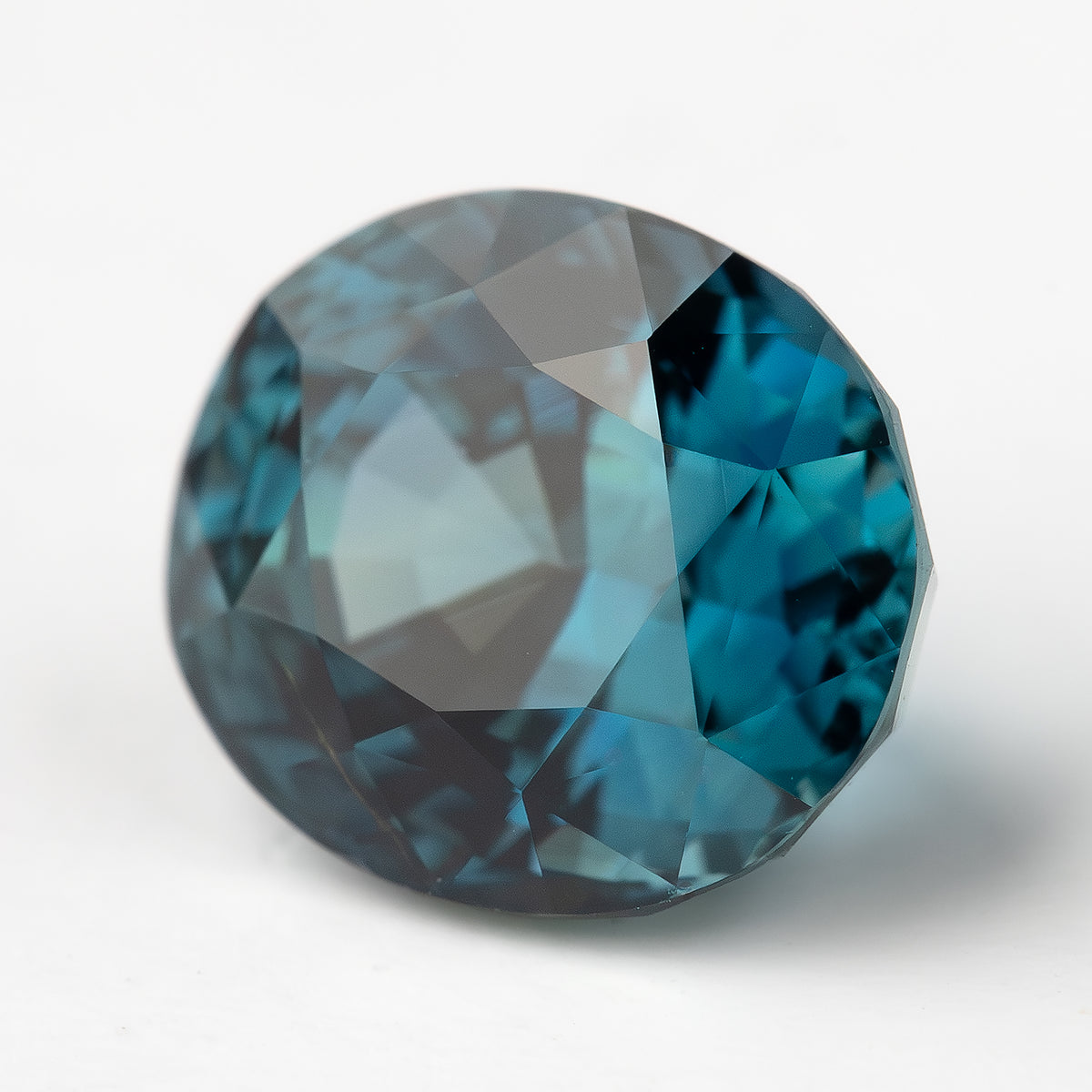 Close tilted view of the oval teal-blue sapphire with bright table reflections and darker edges.