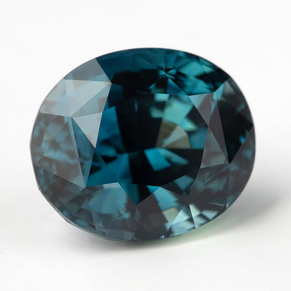 Wider face-up view of the oval teal-blue sapphire on white, showing its rounded outline.