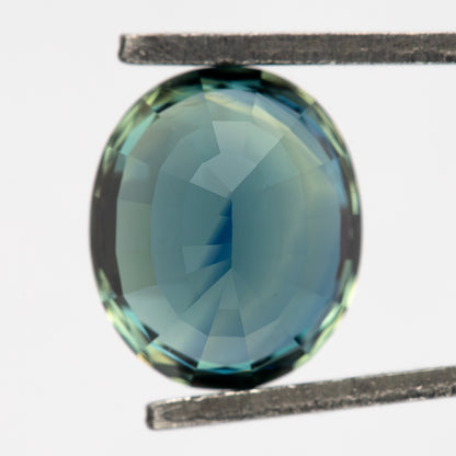 Oval sapphire held pavilion-side forward in tweezers, showing a pale blue-green centre.
