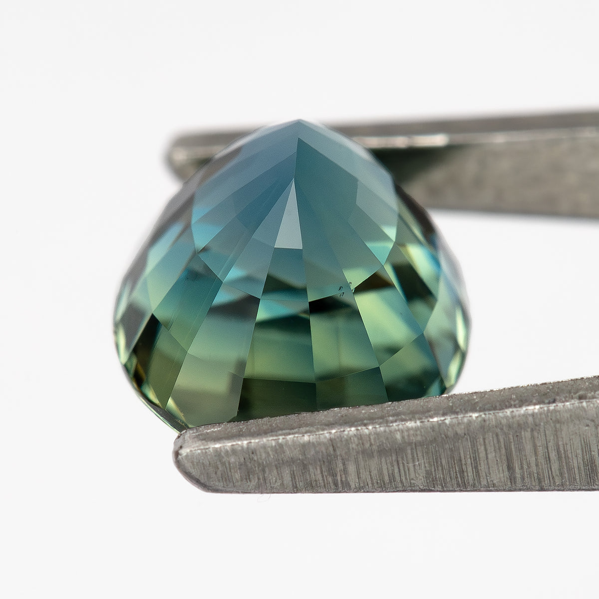 Side view of the oval sapphire in tweezers, showing the pointed pavilion and pale green-blue facets.