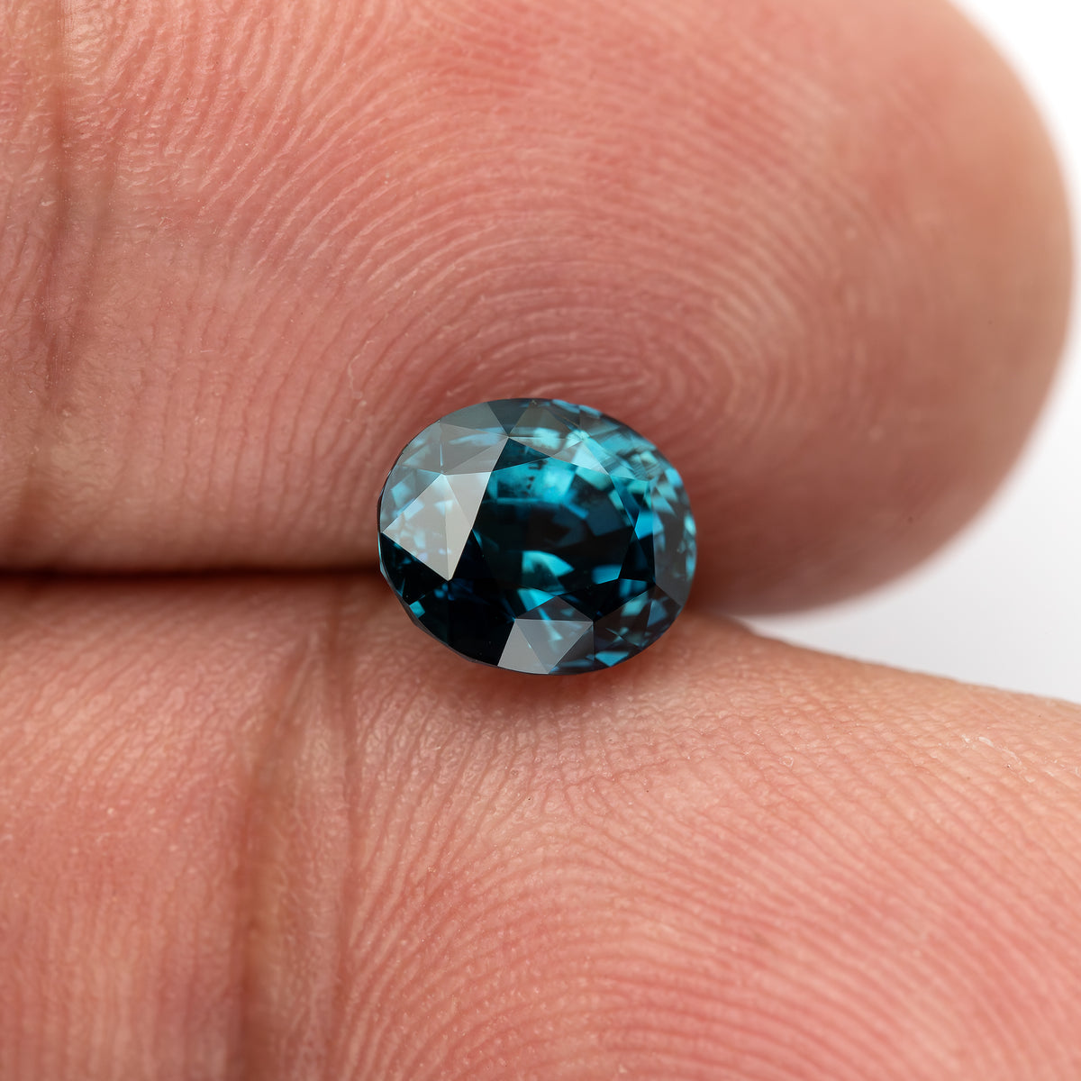 Wider fingertip view of the oval teal-blue sapphire showing its face-up size relative to a finger.