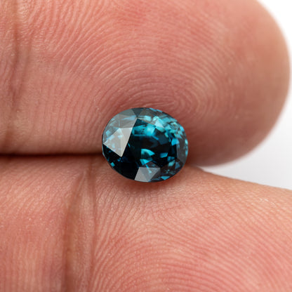 Wider fingertip view of the oval teal-blue sapphire showing its face-up size relative to a finger.