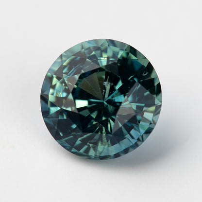 Round deep teal sapphire viewed face up, displaying a mix of blue and green hues.