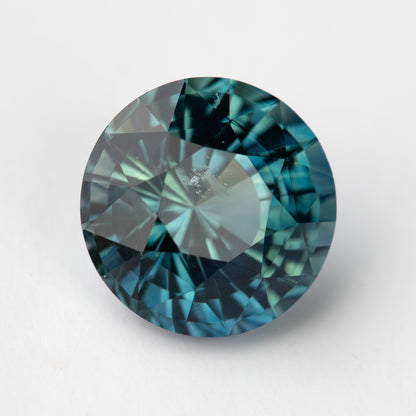 Round deep teal sapphire viewed face up, showcasing a mix of blue and green hues.