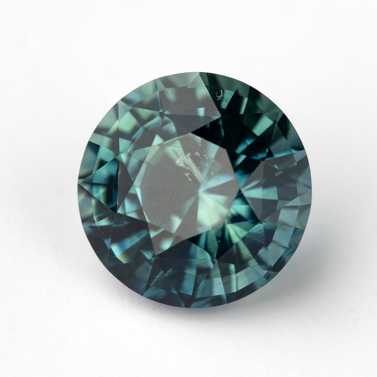 Round, deep teal-blue-green sapphire viewed face up with visible facets.
