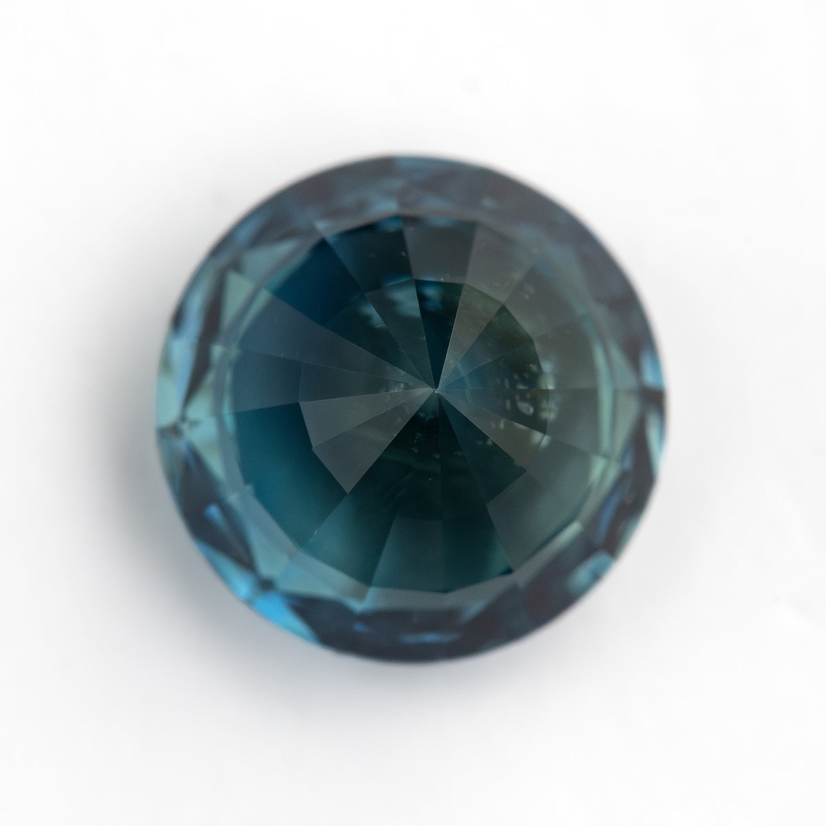 Round deep teal blue-green natural sapphire shown face-up on a white background.