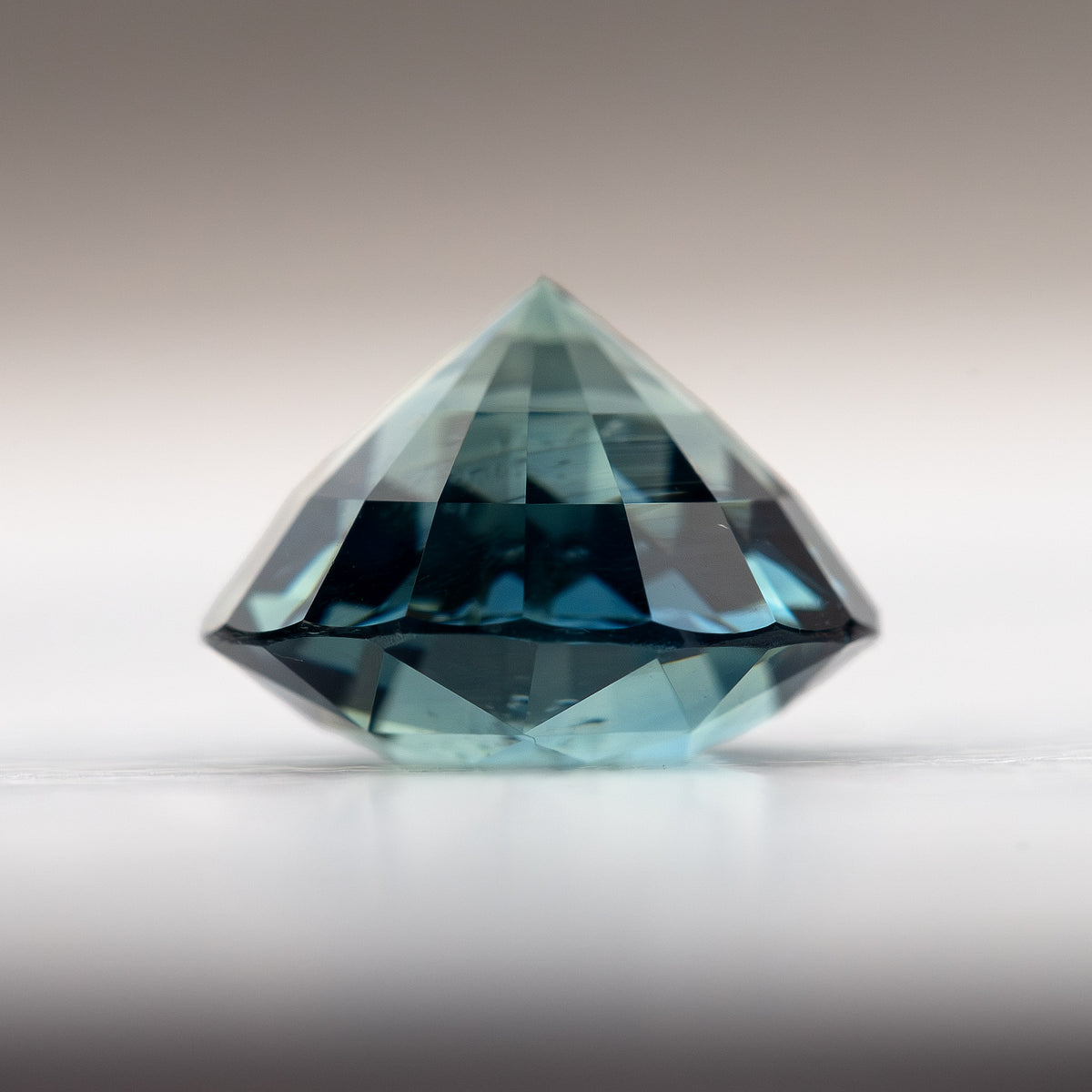 Side view of a 1.85 ct deep teal blue-green sapphire, showcasing its faceted shape and rich color.