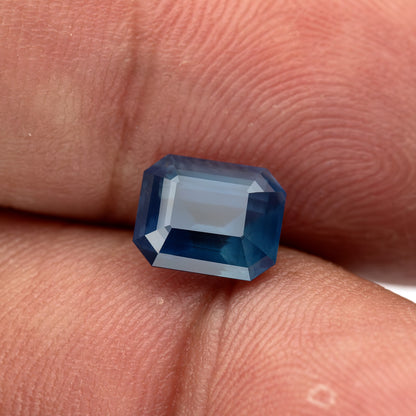 Zafiro sobre las puntas de los dedos bajo un reflejo más brillante, mostrando una respuesta azul más clara a través de la tabla y las facetas escalonadas de la corona.