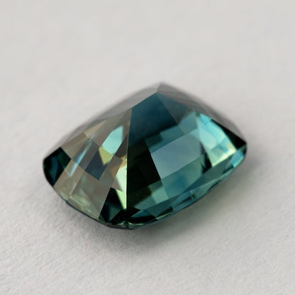 Three-quarter view of the sapphire resting pavilion-up, showing contrasting dark teal and pale green-blue back facets.