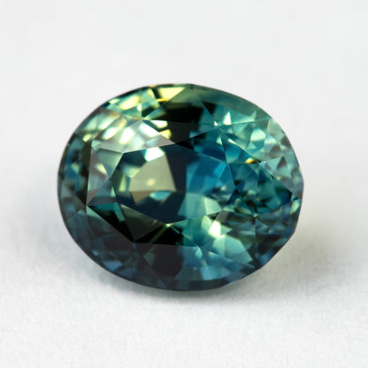 Alternate close face-up view of the oval sapphire, showing bright green-blue flashes and darker teal reflections.