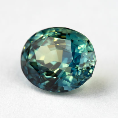 Tilted face-up close-up of the teal sapphire, showing a different reflection pattern across the oval mixed cut.