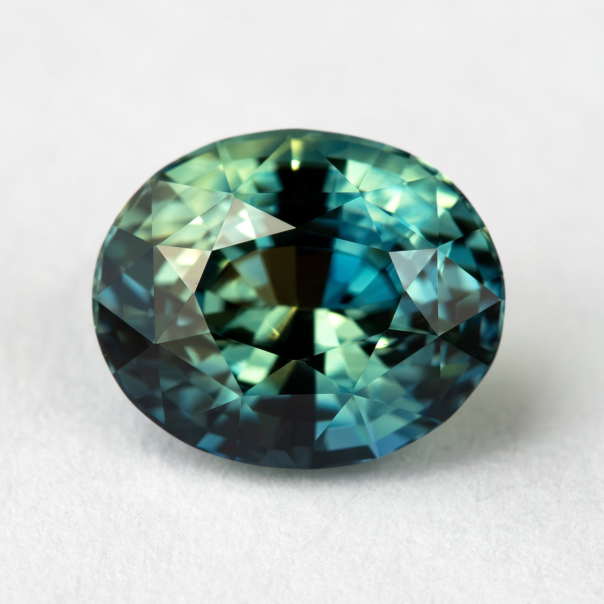 Face-up macro view of the oval sapphire with a broad dark central reflection and brighter teal facets around the edge.