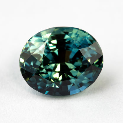 Face-up macro of the oval sapphire, showing deeper teal tone and high-contrast reflections across the mixed cut.