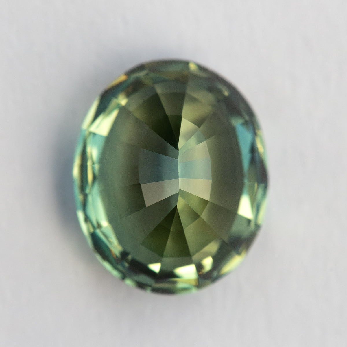 Pavilion-facing view of the oval sapphire, showing the back facet pattern and softer green-blue color.