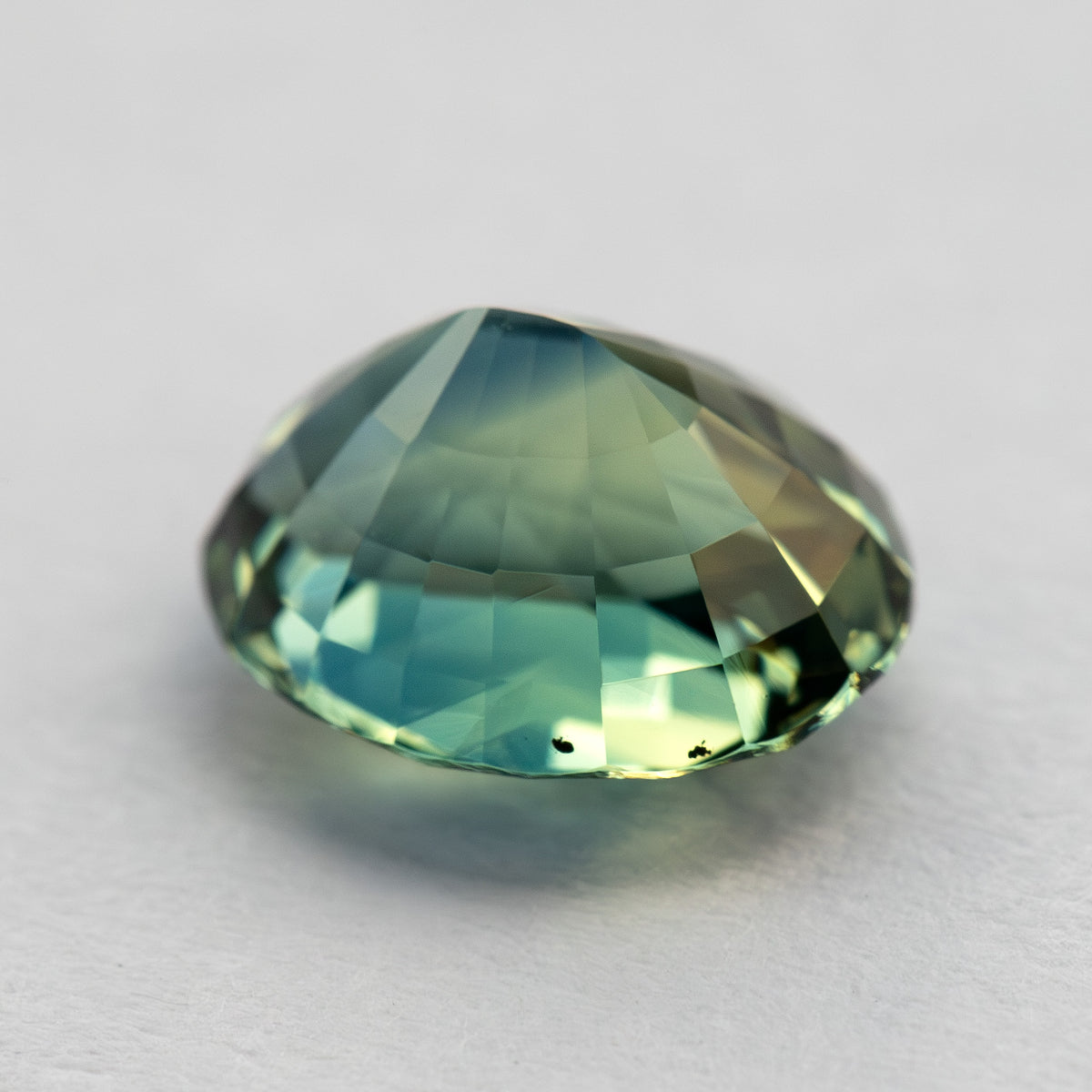 Low side profile of the oval sapphire, showing its pavilion depth and natural internal features near the lower edge.