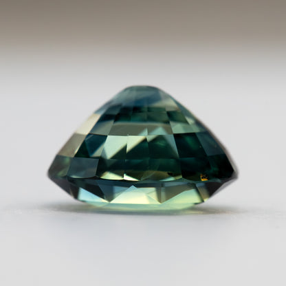 Side profile of the loose oval sapphire, showing the crown, girdle and pavilion depth against a pale background.