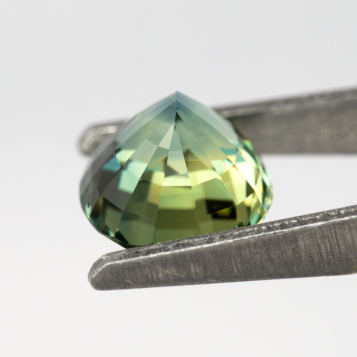 Three-quarter side and pavilion view of the sapphire, showing the girdle, pavilion shape and green reflections.
