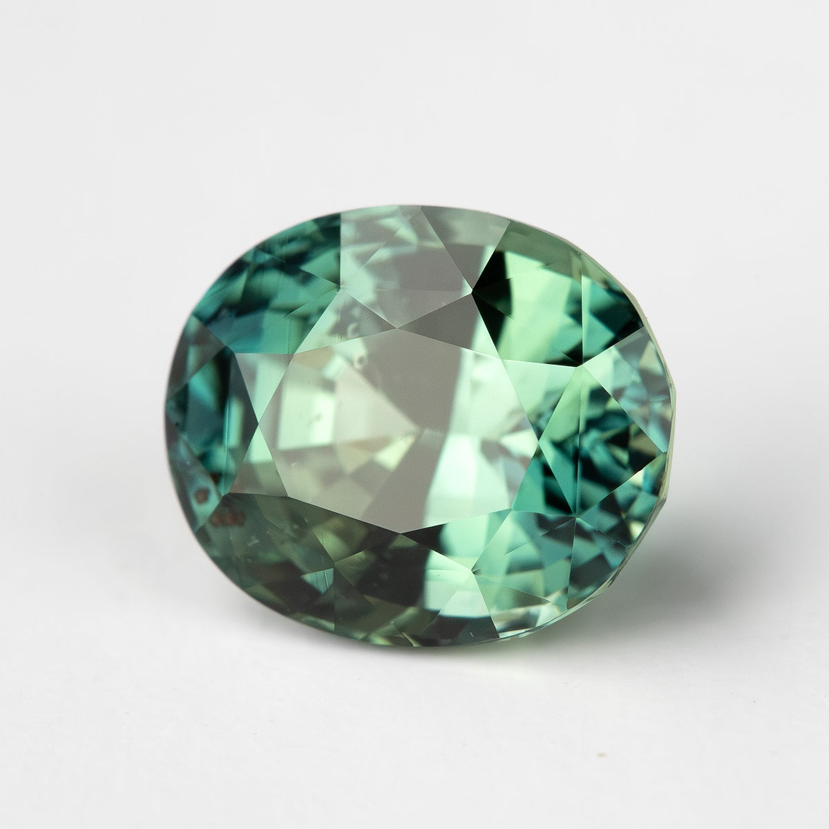Oval-shaped teal blue-green sapphire, face-up view, highlighting its facets on a white background.