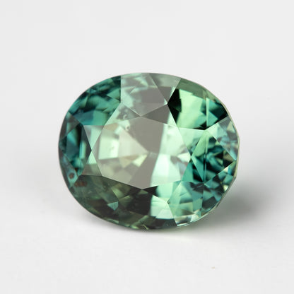 Oval-shaped teal blue-green sapphire, face-up view, highlighting its facets on a white background.