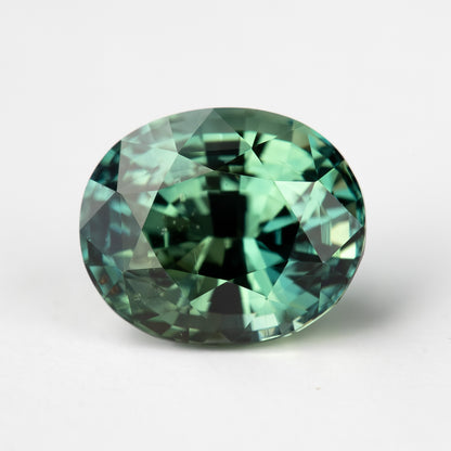 Oval-shaped teal blue-green sapphire gemstone displayed face-up.
