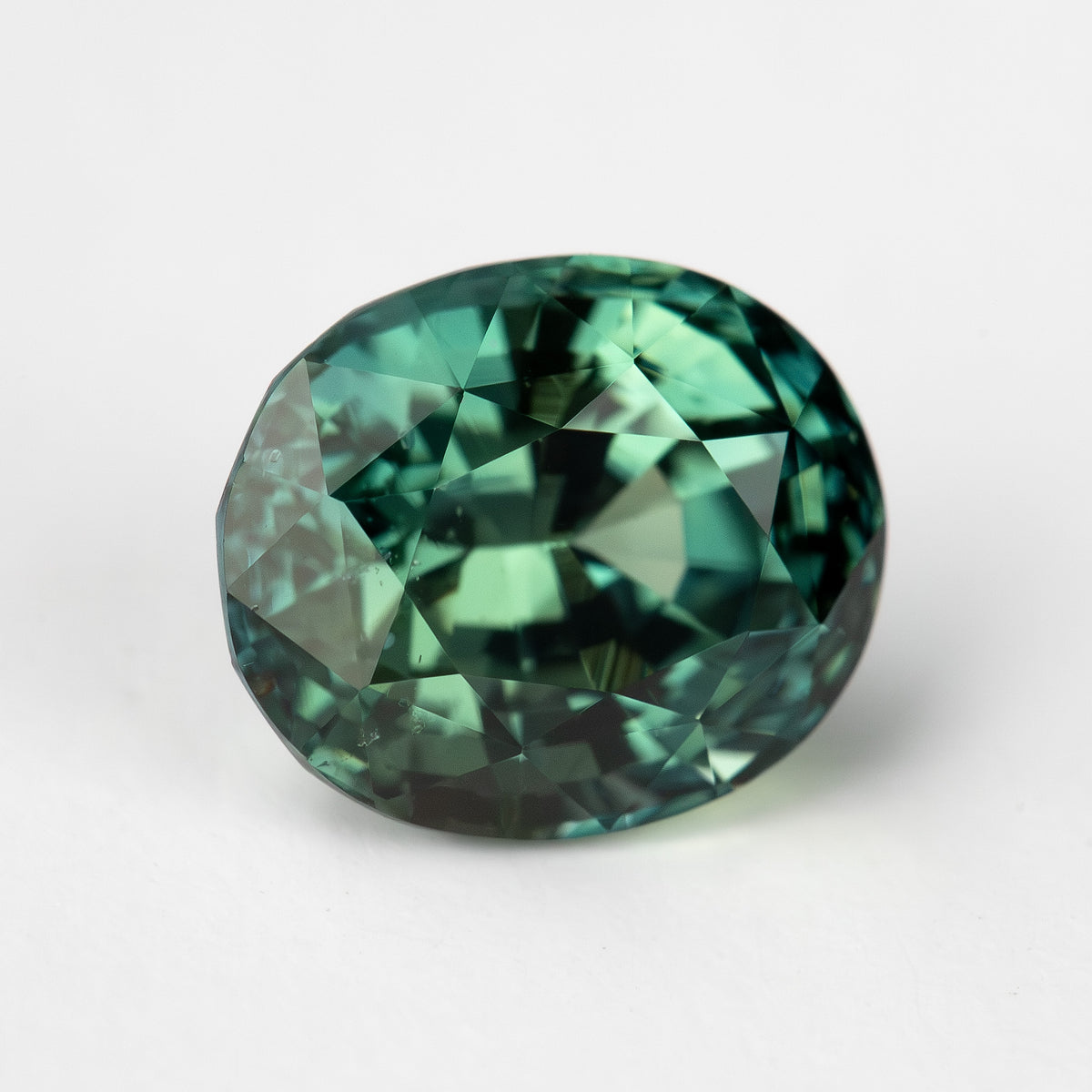Oval-shaped teal blue-green sapphire displayed face-up on a white background.