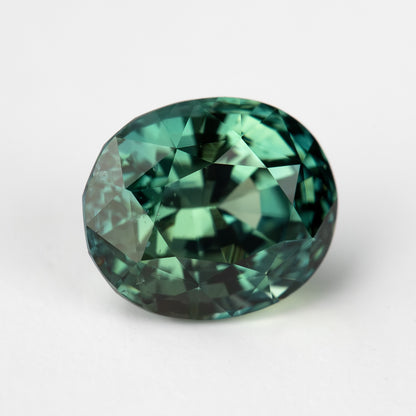 Oval-shaped teal blue-green sapphire displayed face-up on a white background.