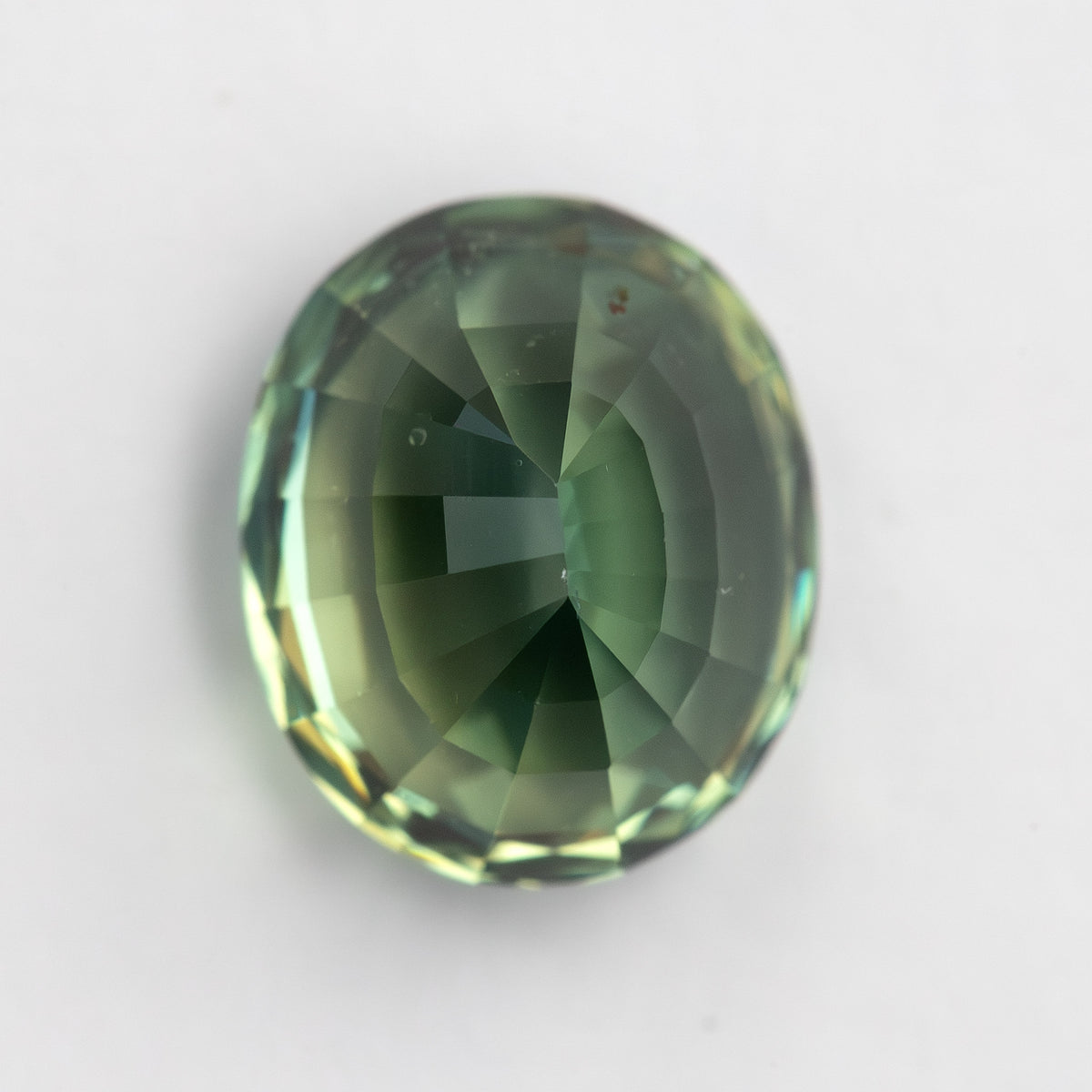 Oval mixed-cut teal blue-green sapphire viewed face-up on a plain background.