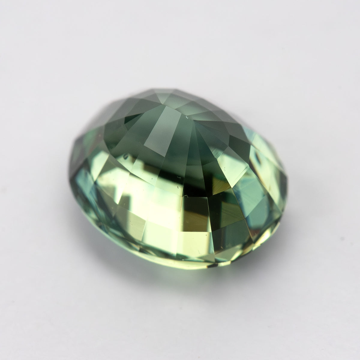 Oval-shaped teal blue-green sapphire shown from the side on a white background.