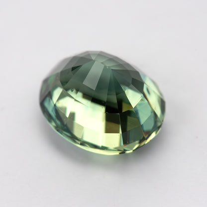 Oval-shaped teal blue-green sapphire shown from the side on a white background.