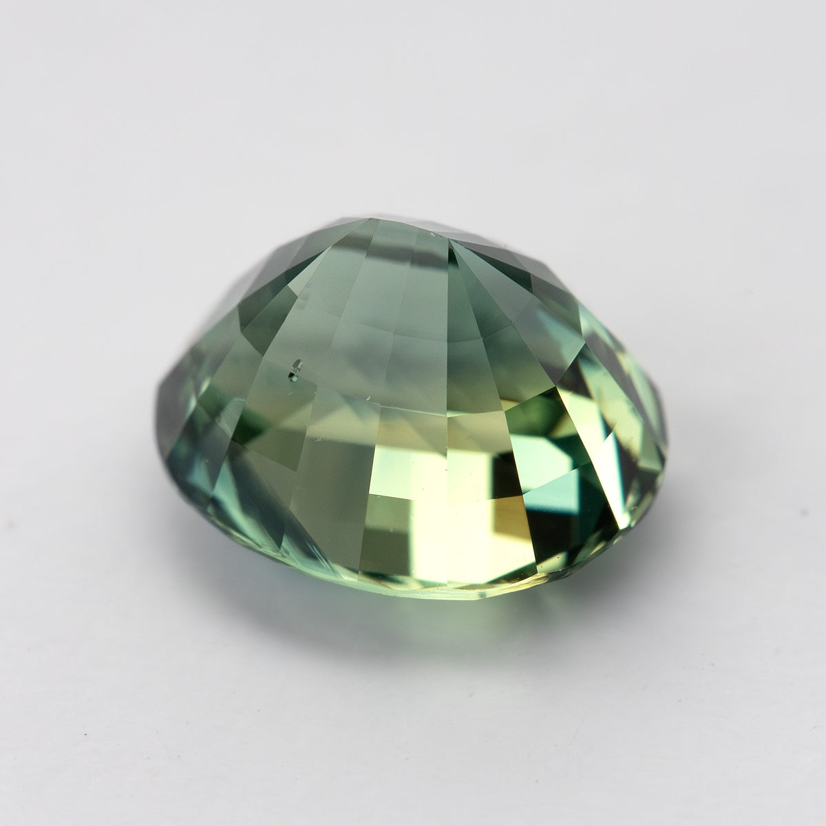 Oval teal blue-green sapphire viewed from side, showcasing its facets against a plain background.