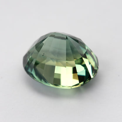 Oval teal blue-green sapphire viewed from side, showcasing its facets against a plain background.