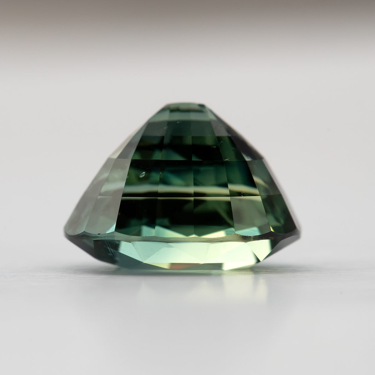 Teal blue-green natural sapphire shown from the side, displaying its multifaceted shape and color depth.