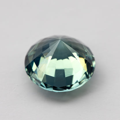 Teal blue-green round step-cut sapphire shown at an angle from the pavilion side. View 13.