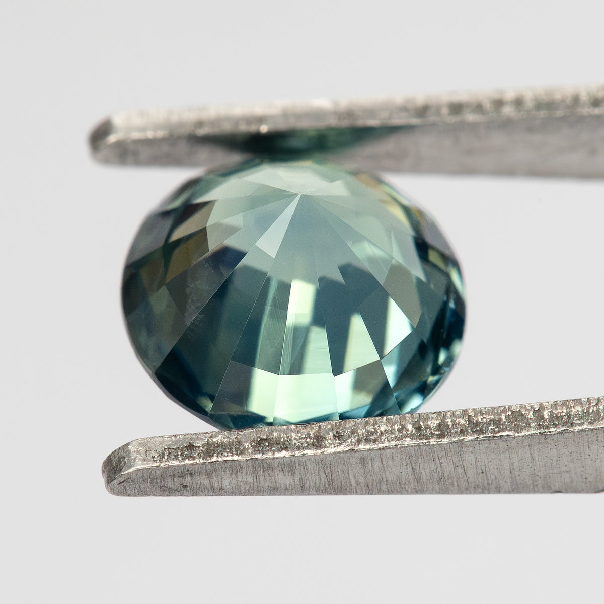Teal blue-green round step-cut sapphire shown at an angle from the pavilion side. View 16.
