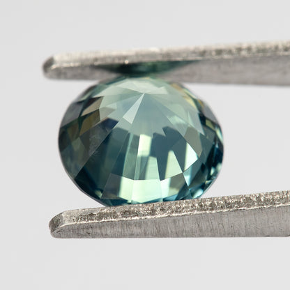 Teal blue-green round step-cut sapphire shown at an angle from the pavilion side. View 16.