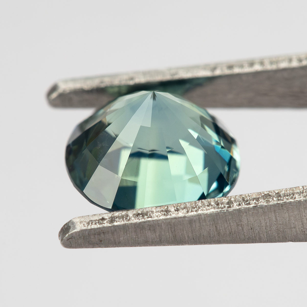 Teal blue-green round step-cut sapphire shown at an angle from the pavilion side. View 17.