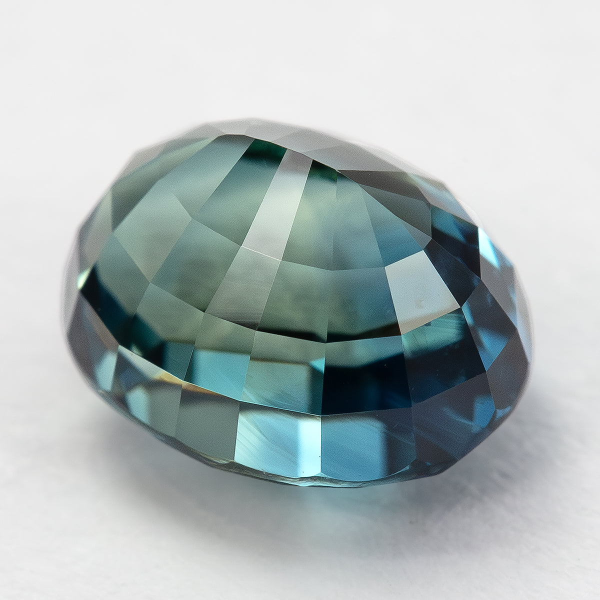 Angled pavilion view of the oval sapphire, showing its depth above a pale surface.