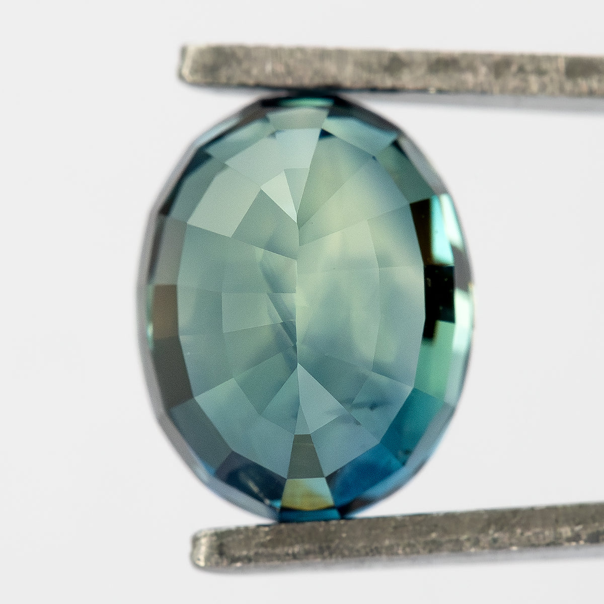 Reverse view of oval sapphire held in tweezers against a pale background.