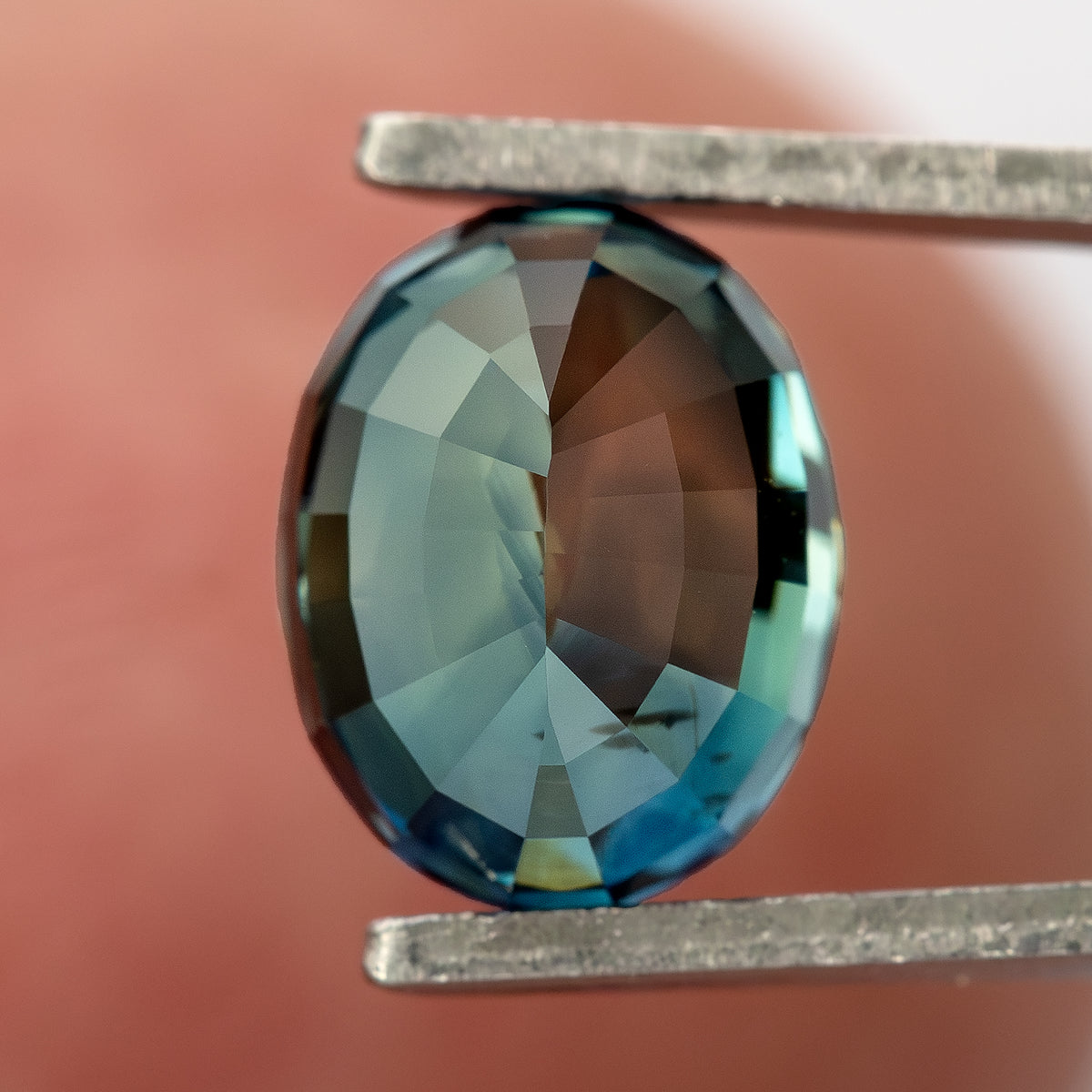 Reverse view of sapphire in tweezers against a blurred finger background.