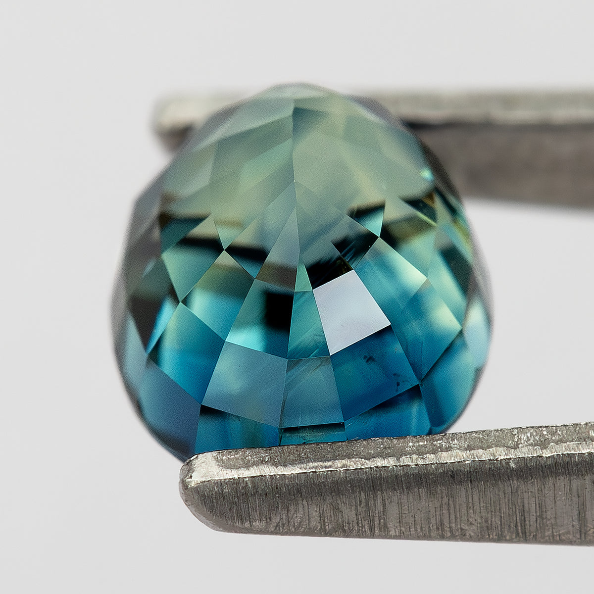 Oblique pavilion view of the oval sapphire held in tweezers.