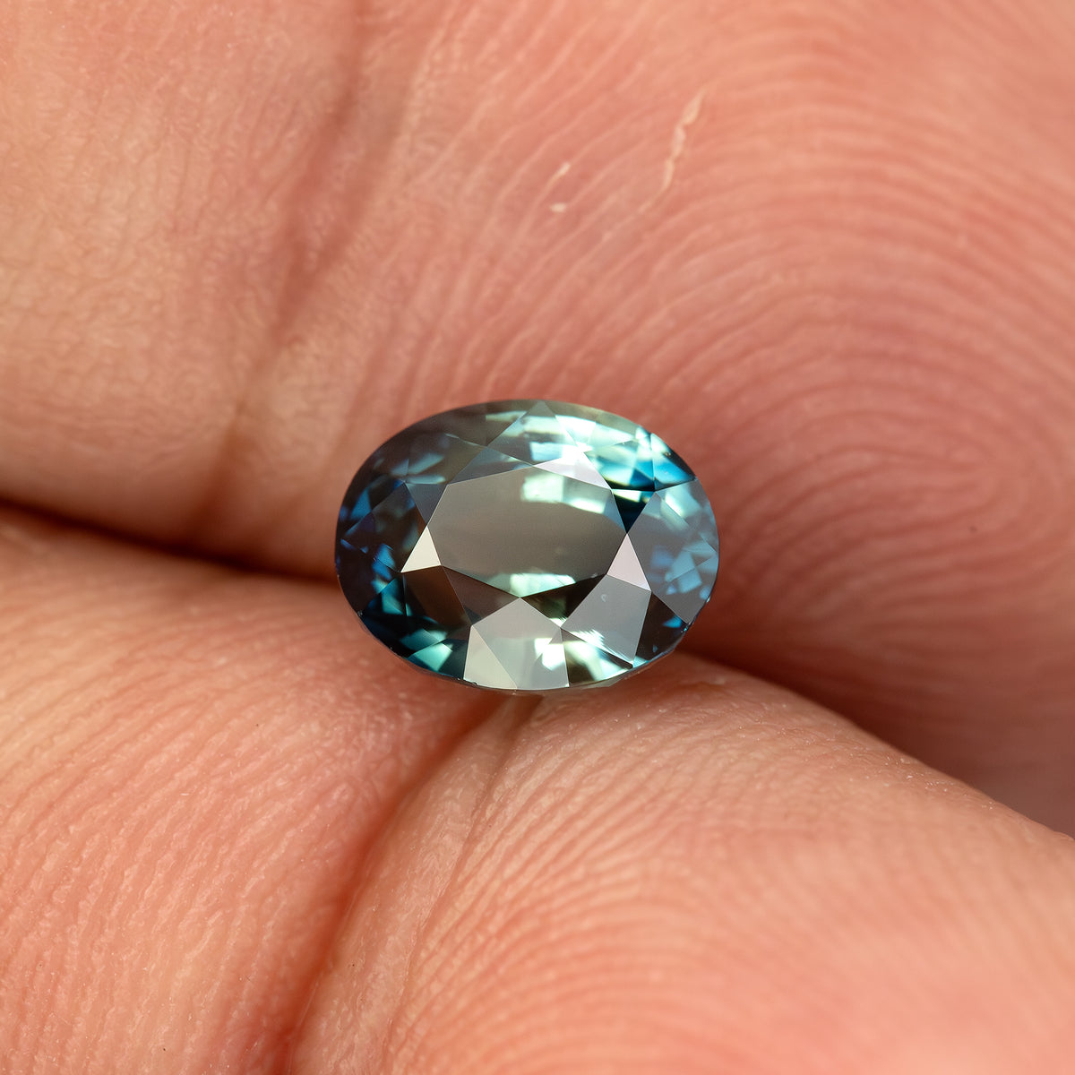 Oval sapphire resting face-up between fingertips, showing its size and facet reflections.