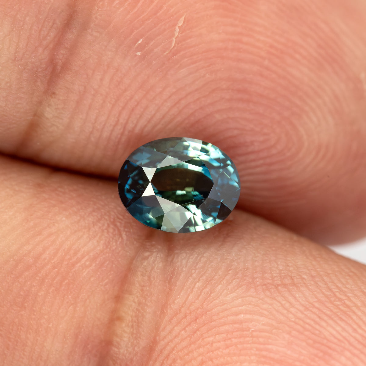 Face-up oval sapphire against fingertips from an alternate angle.