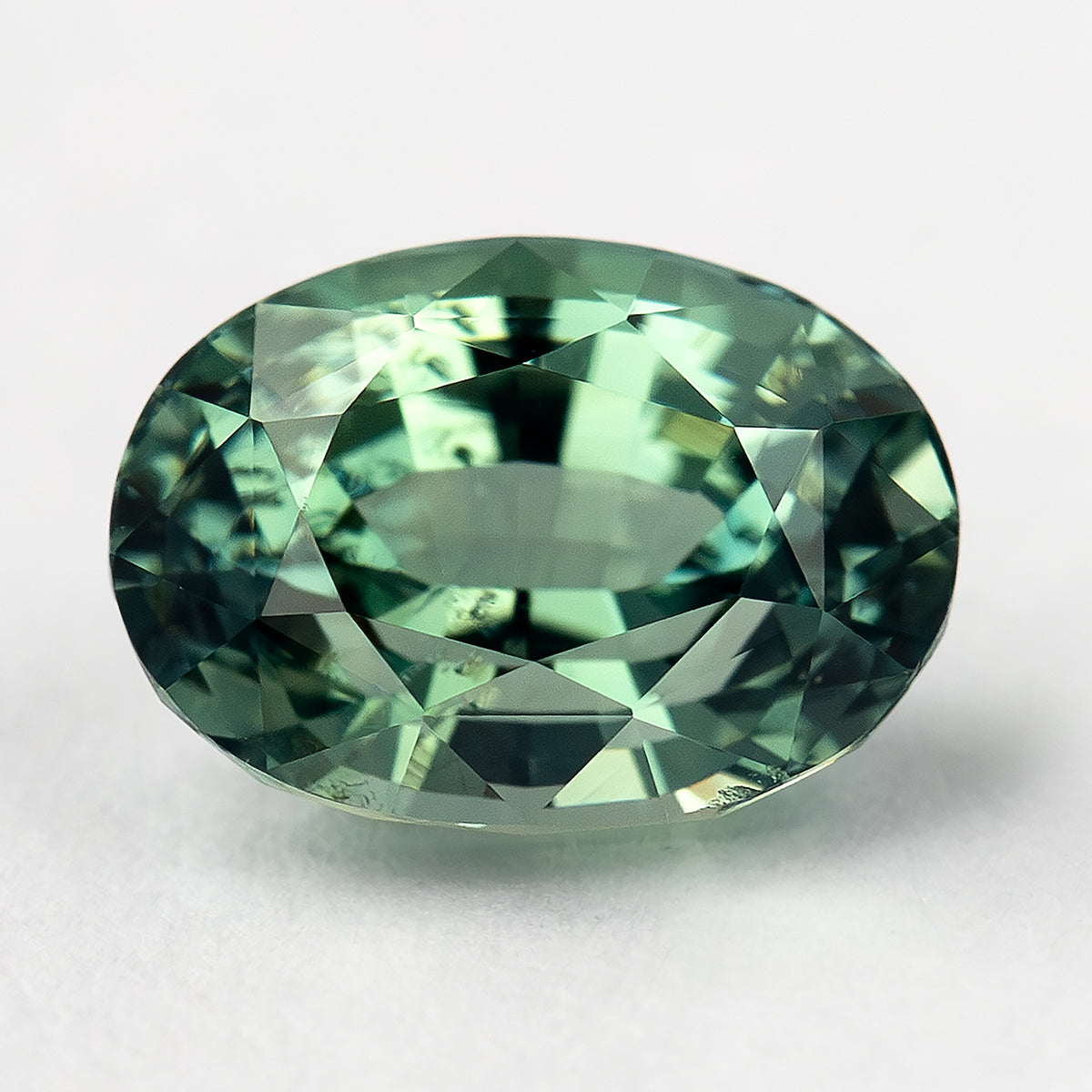Face-up macro of the teal-green oval sapphire, showing the broad central table and complete outline.